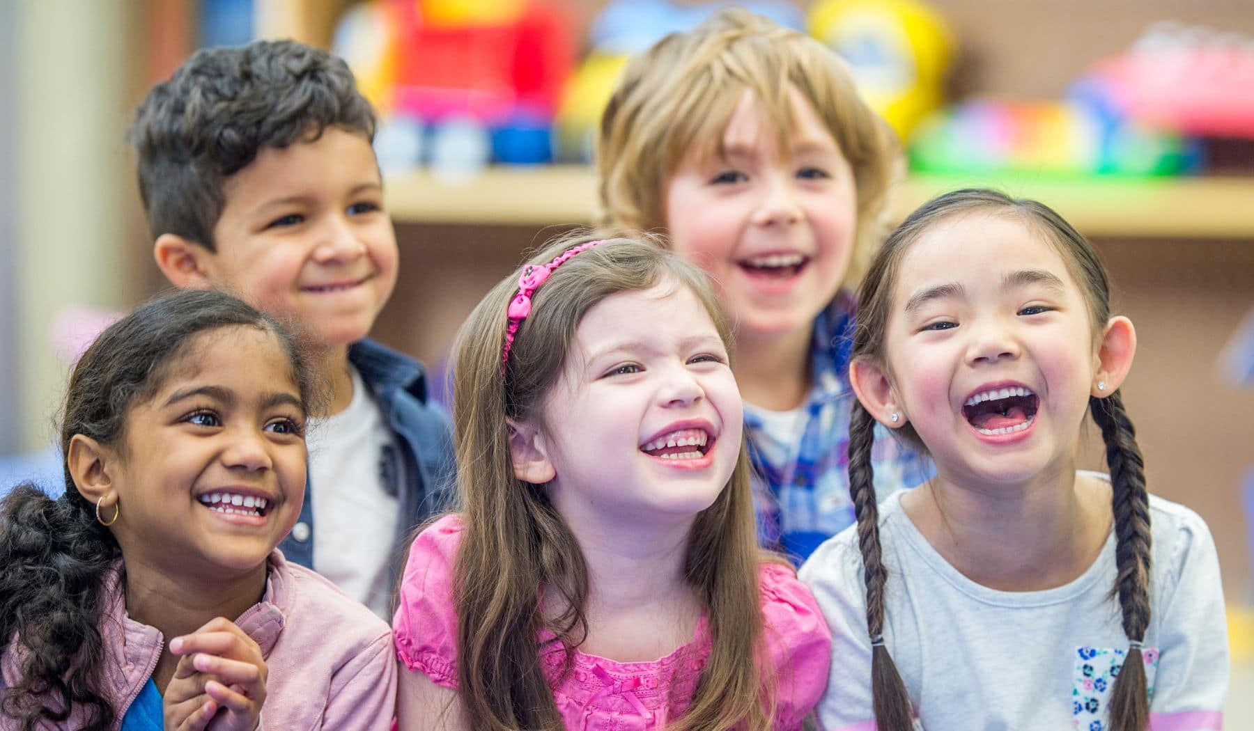 Five young children laughing in a classroom